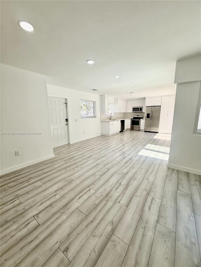 unfurnished living room with a sink, baseboards, light wood-style floors, and recessed lighting