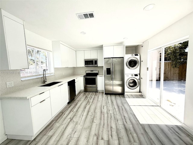 kitchen featuring visible vents, a sink, backsplash, appliances with stainless steel finishes, and stacked washer / dryer