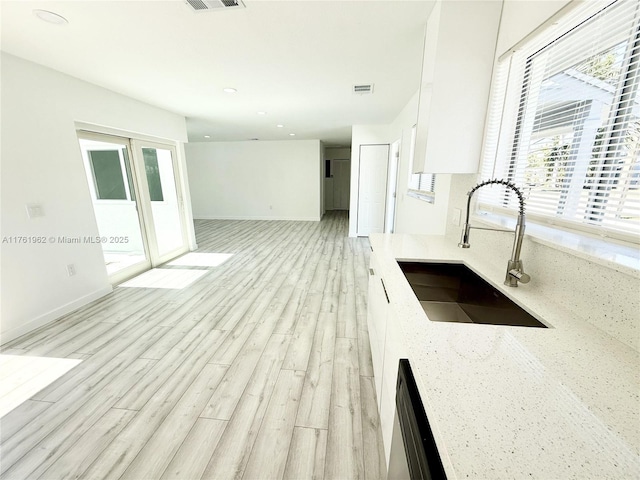 kitchen with visible vents, light stone countertops, dishwasher, light wood-style floors, and a sink