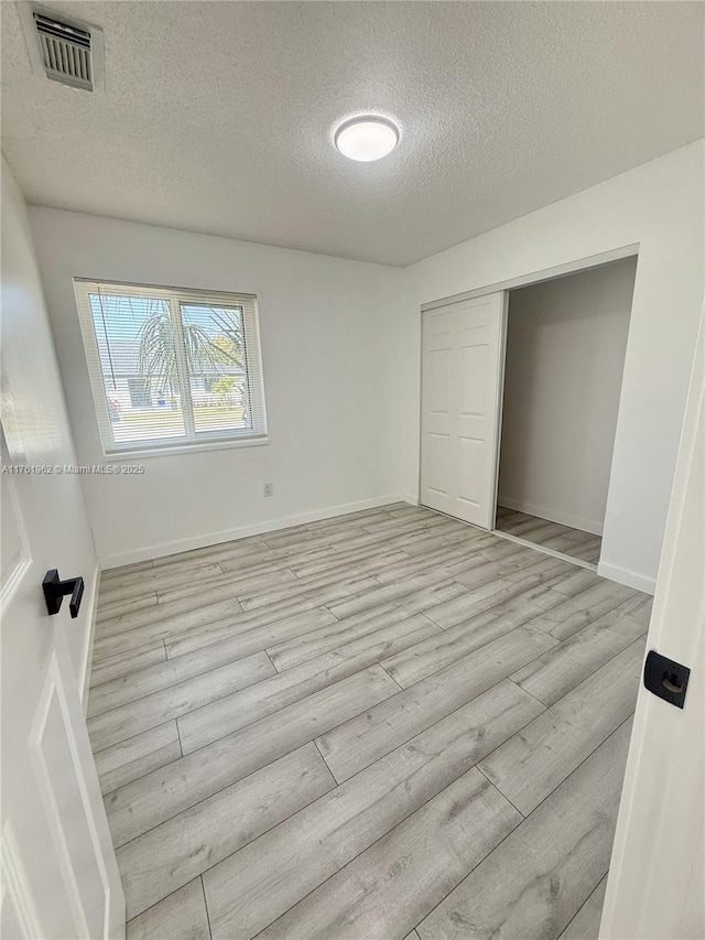 unfurnished bedroom featuring visible vents, a textured ceiling, a closet, light wood-style floors, and baseboards