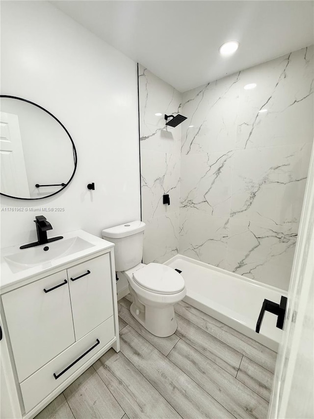 bathroom featuring a marble finish shower, toilet, vanity, and wood finished floors