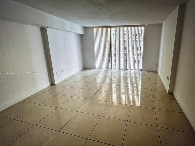 tiled empty room featuring a wall of windows, baseboards, and a textured ceiling