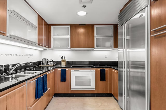 kitchen with white oven, dark countertops, built in refrigerator, and a sink