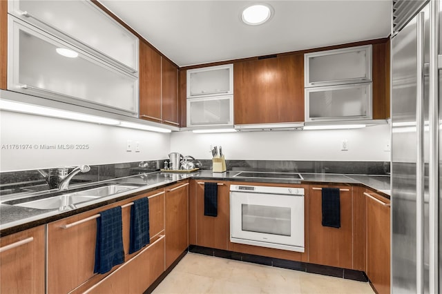 kitchen with brown cabinetry, a sink, stainless steel built in fridge, oven, and black electric stovetop