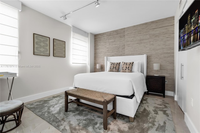 bedroom featuring an accent wall, rail lighting, and baseboards