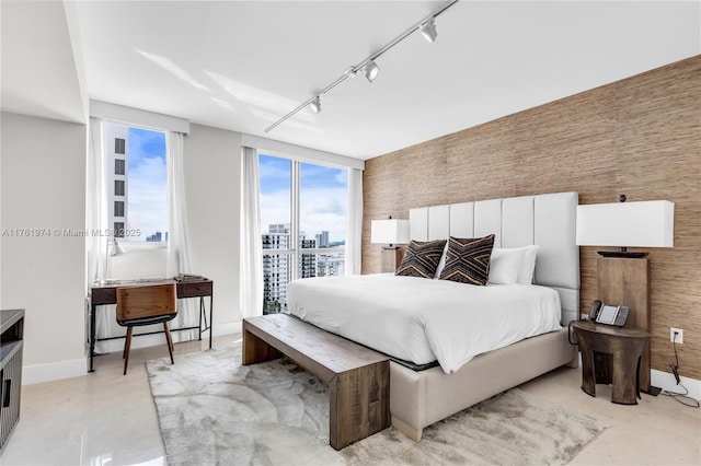 bedroom featuring a city view, finished concrete floors, rail lighting, baseboards, and an accent wall