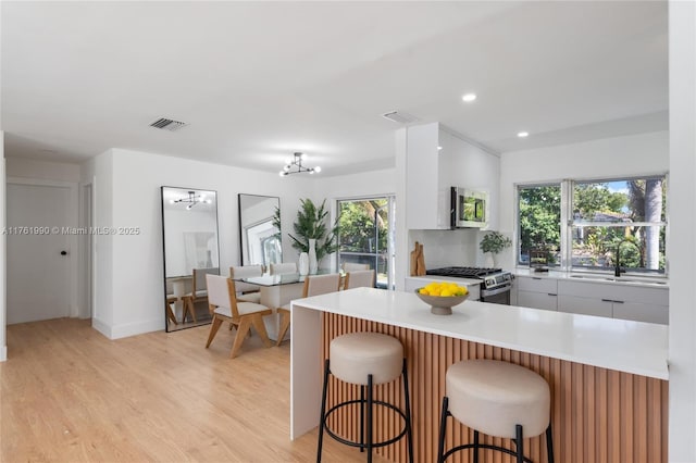 kitchen featuring a breakfast bar area, visible vents, light wood-style flooring, light countertops, and appliances with stainless steel finishes