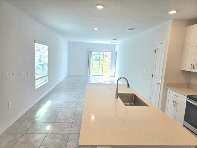 kitchen with light tile patterned floors, visible vents, a kitchen island with sink, a sink, and white cabinets