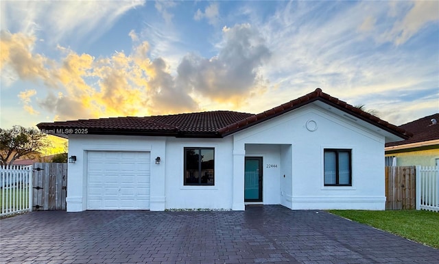 view of front of property with stucco siding, decorative driveway, fence, an attached garage, and a tiled roof