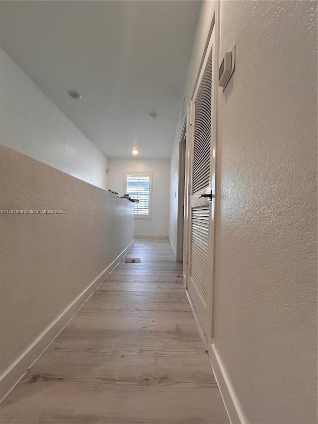 hall with light wood finished floors, baseboards, and a textured wall