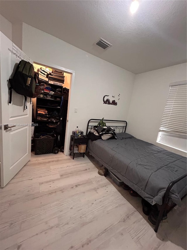 bedroom featuring visible vents, light wood-style flooring, a closet, a textured ceiling, and a walk in closet