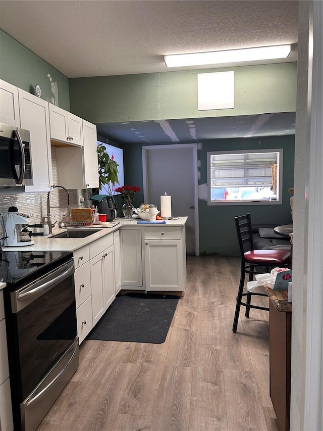 kitchen with light countertops, stainless steel appliances, wood finished floors, white cabinetry, and a sink