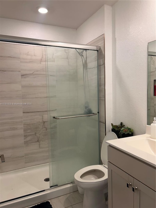 bathroom featuring a shower stall, toilet, vanity, and a textured wall