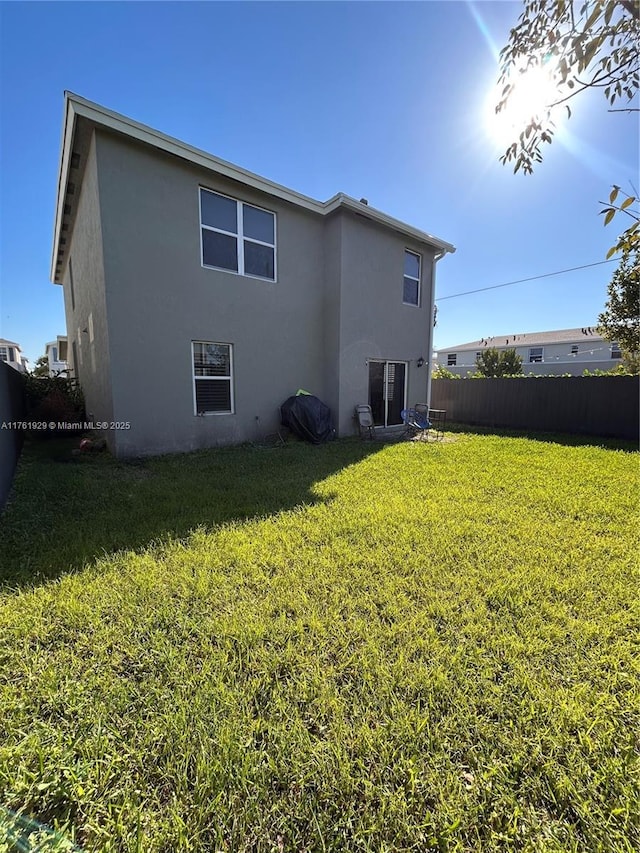 rear view of house with a yard, fence, and stucco siding