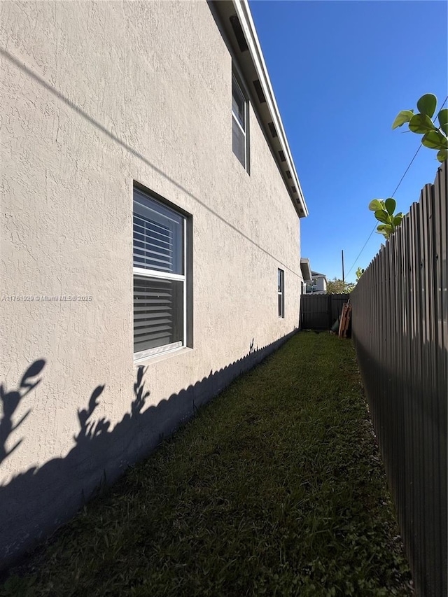 view of side of property featuring a yard, stucco siding, and a fenced backyard