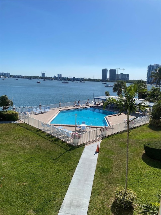 community pool with a patio, a yard, fence, and a water view