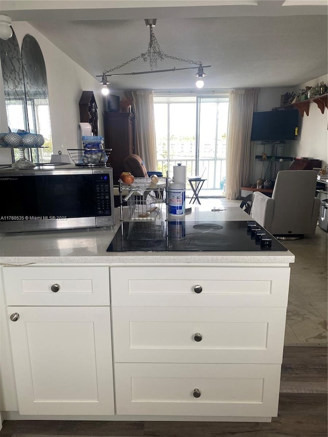 kitchen featuring stainless steel microwave, black electric stovetop, open floor plan, and white cabinetry