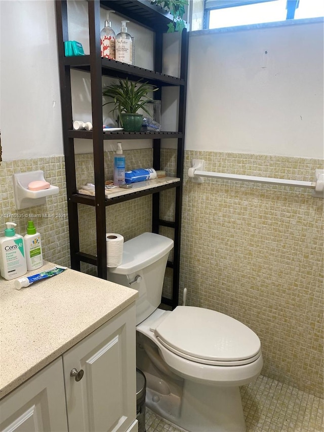 bathroom featuring toilet, tile walls, wainscoting, tile patterned flooring, and vanity