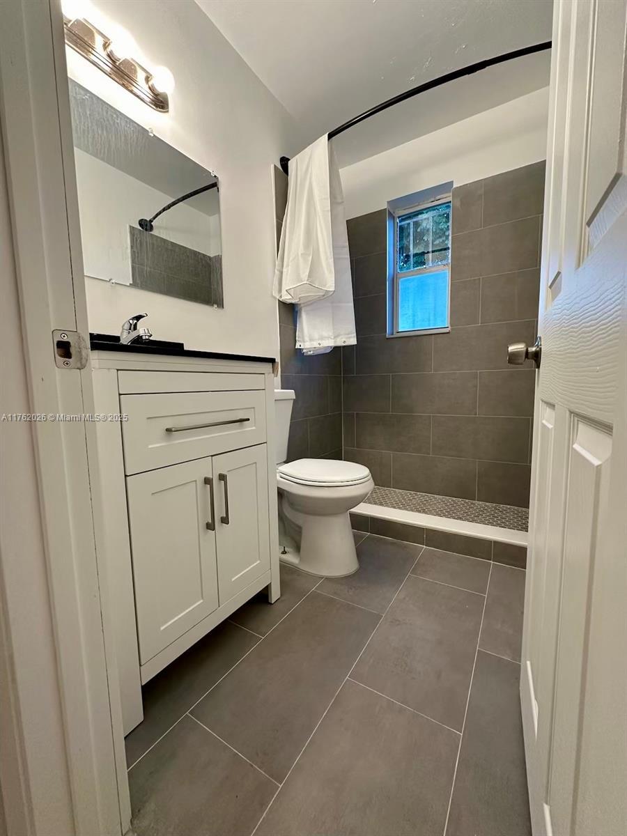 full bathroom featuring a tile shower, tile patterned floors, toilet, and vanity