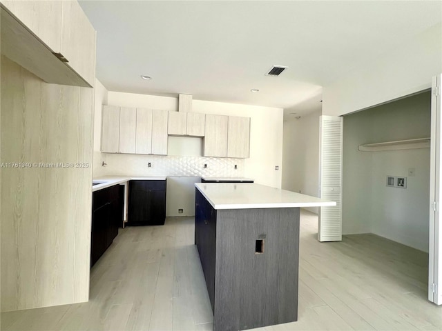 kitchen featuring light wood-style floors, decorative backsplash, a center island, and visible vents