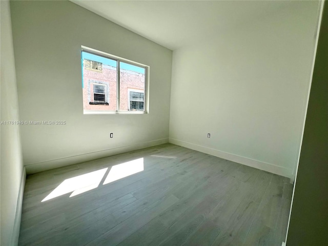 spare room with baseboards and wood finished floors