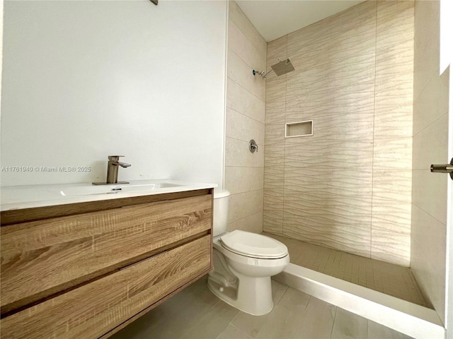 bathroom featuring a tile shower, vanity, tile patterned flooring, and toilet