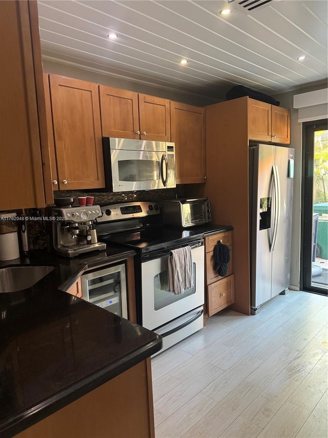 kitchen with a sink, light wood-style floors, appliances with stainless steel finishes, dark countertops, and brown cabinets