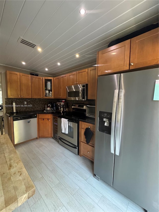 kitchen with visible vents, glass insert cabinets, appliances with stainless steel finishes, brown cabinets, and backsplash