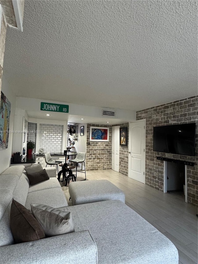 living area featuring wood finished floors, visible vents, brick wall, and a textured ceiling