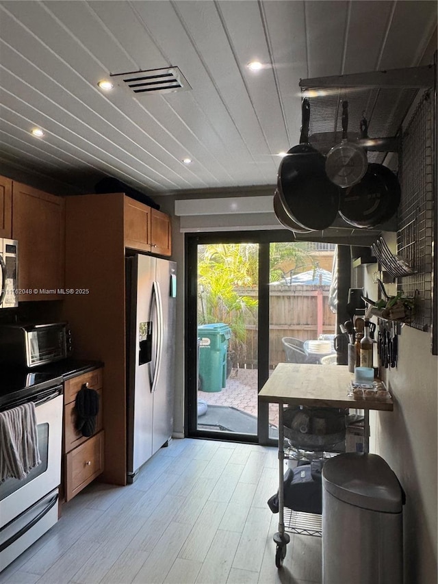 kitchen with brown cabinetry, visible vents, a toaster, light wood-style floors, and appliances with stainless steel finishes