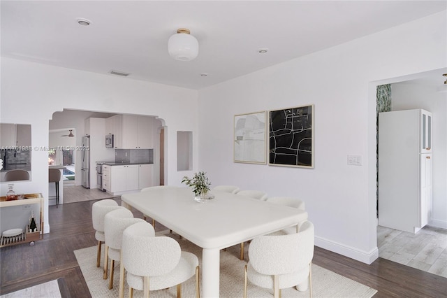 dining area featuring light wood finished floors, visible vents, arched walkways, and baseboards