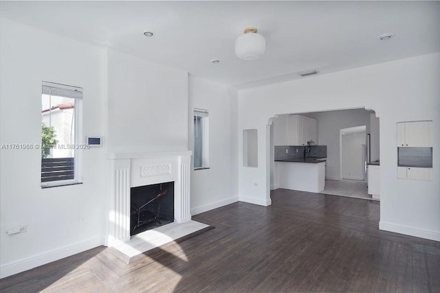 unfurnished living room featuring a fireplace, dark wood-style floors, visible vents, and baseboards