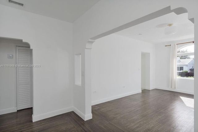 empty room featuring visible vents, baseboards, and dark wood finished floors