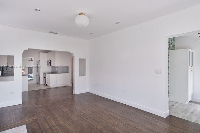 unfurnished living room with arched walkways, visible vents, baseboards, and wood finished floors