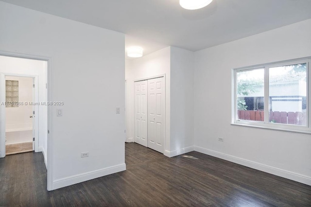 unfurnished bedroom with a closet, baseboards, and dark wood-style flooring