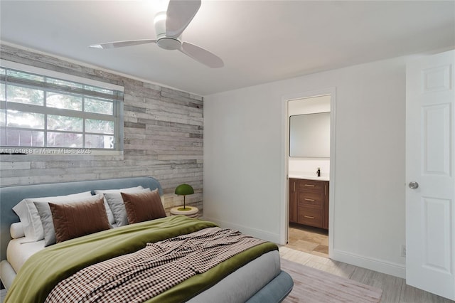 bedroom featuring wooden walls, baseboards, a sink, ensuite bathroom, and an accent wall