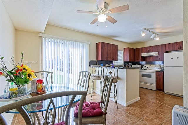 kitchen with a ceiling fan, under cabinet range hood, a textured ceiling, white appliances, and a peninsula