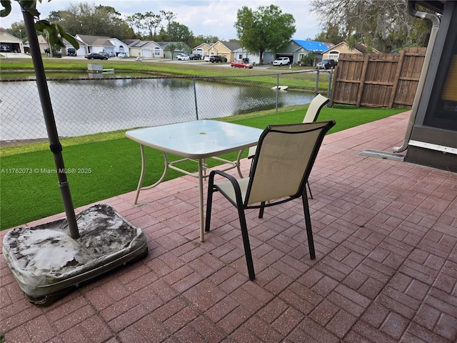 view of patio / terrace featuring outdoor dining area, a residential view, fence, and a water view