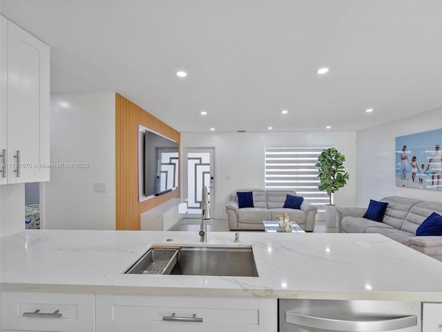 kitchen featuring a sink, light stone countertops, open floor plan, and white cabinets