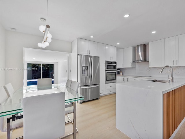 kitchen with a sink, white cabinetry, stainless steel appliances, wall chimney exhaust hood, and light wood finished floors