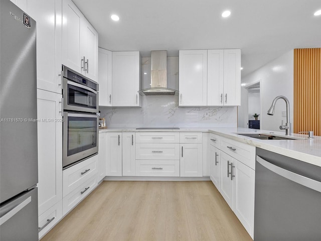 kitchen with tasteful backsplash, light wood-style flooring, stainless steel appliances, wall chimney exhaust hood, and a sink