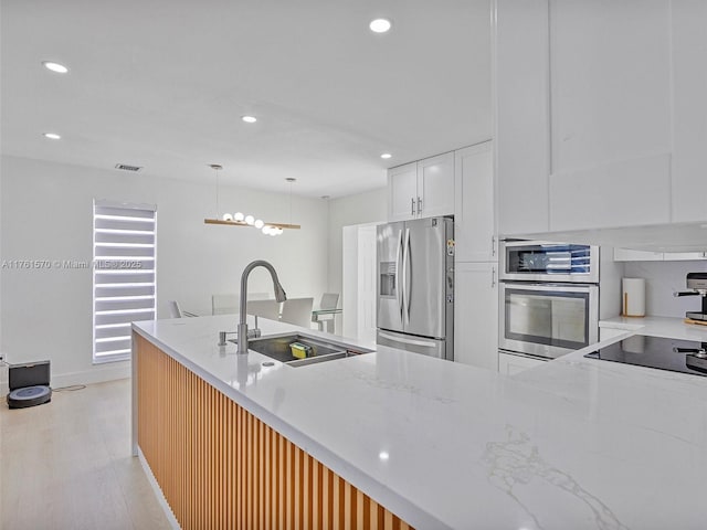 kitchen with a sink, light stone counters, appliances with stainless steel finishes, and white cabinets