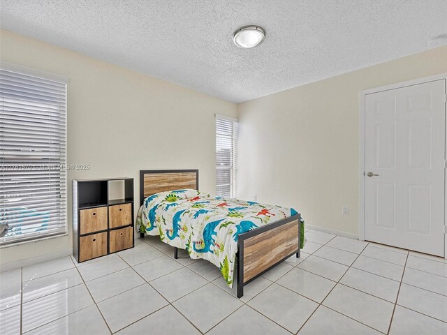 bedroom with baseboards, a textured ceiling, and light tile patterned flooring