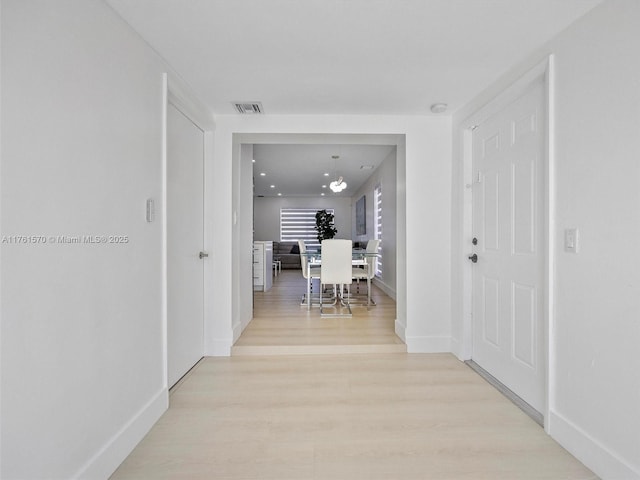 hallway featuring light wood finished floors, visible vents, and baseboards