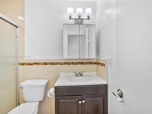 bathroom featuring a shower with door, toilet, vanity, and tile walls