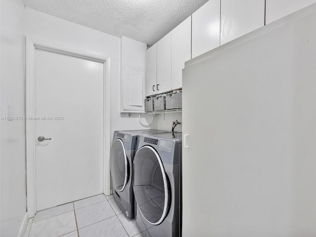 clothes washing area with electric panel, light tile patterned flooring, cabinet space, a textured ceiling, and washer and clothes dryer