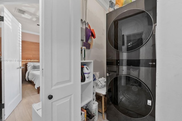 laundry room featuring visible vents, stacked washer and clothes dryer, ornamental molding, wood finished floors, and laundry area