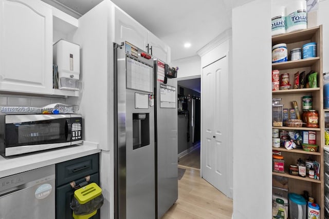 kitchen with light wood finished floors, ornamental molding, light countertops, appliances with stainless steel finishes, and white cabinetry