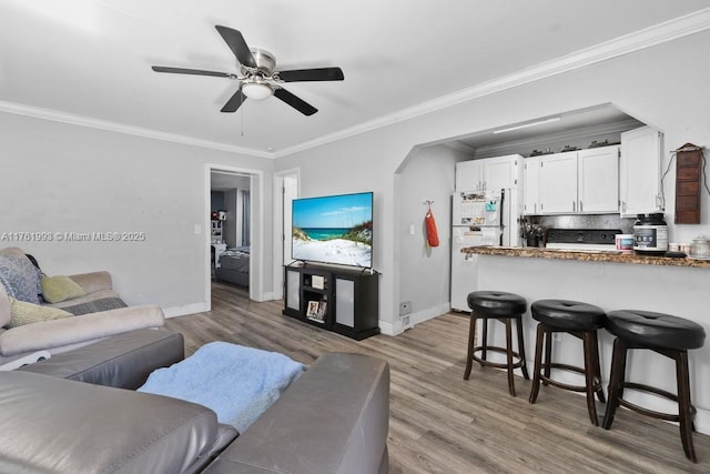 living area featuring light wood-type flooring, baseboards, ceiling fan, and crown molding