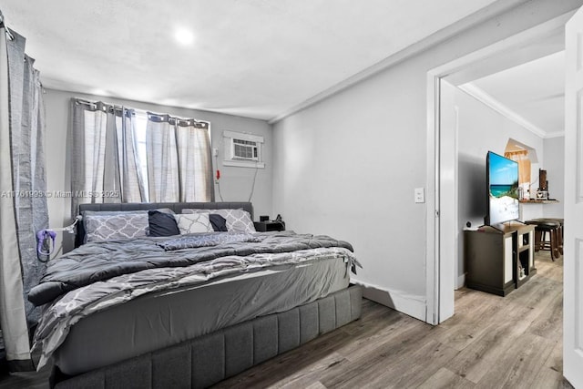 bedroom with ornamental molding, an AC wall unit, baseboards, and wood finished floors